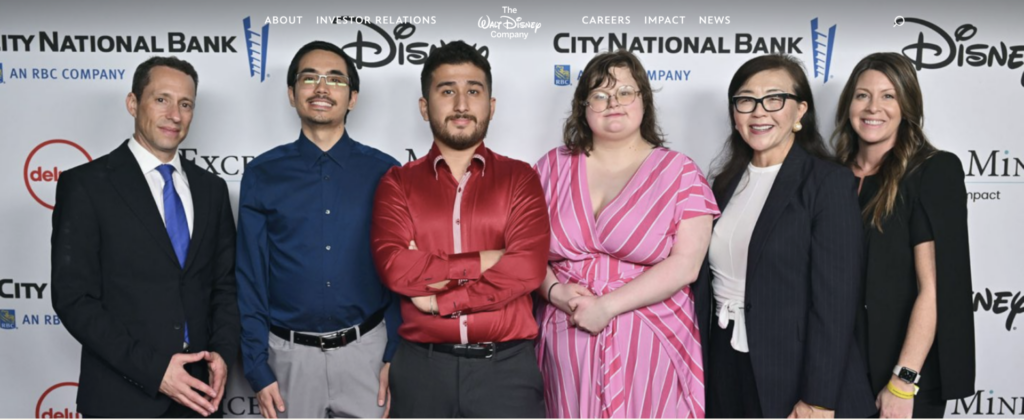Photo of Exceptional Minds staff, students, and alumni in front of a Disney step-and-repeat